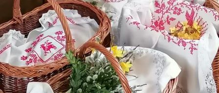 Mehrere Korbweidenkörbe mit weißen Tüchern und Blumen sind auf einem roten Teppich platziert. Ein weißer Tischläufer bedeckt einen Tisch auf der linken Seite. Hinter dem Tisch befindet sich eine weiße Wand mit einem Gegenstand oben.