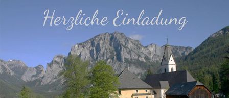 Ein gelbes Haus mit einem Kirchturm steht in einem Dorf, umgeben von grünen Bäumen und Bergen. Die Worte 'Herzliche Einladung' sind oben angebracht.