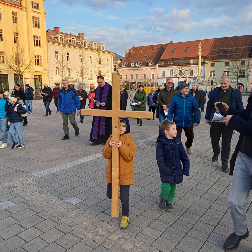 Eine Prozession in einem städtischen Gebiet mit einem Priester und einer Gruppe von Menschen, einschließlich Kinder, die ein Kreuz halten und vorne gehen.