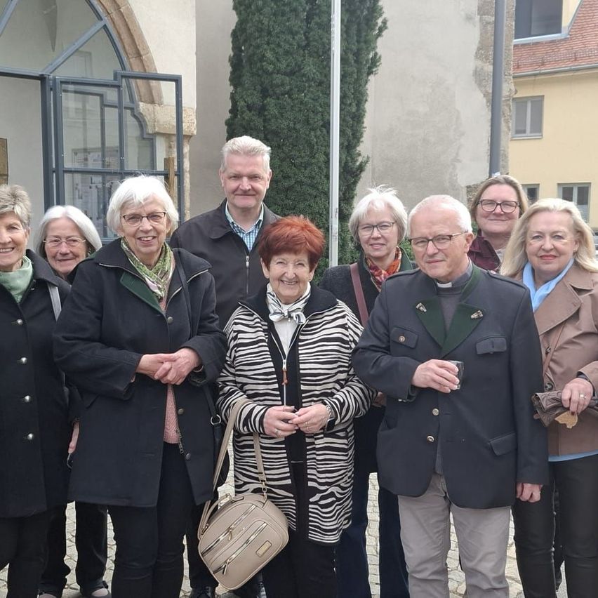 A group of people in formal attire standing outside an old building. A woman in a zebra print jacket smiles in the center.