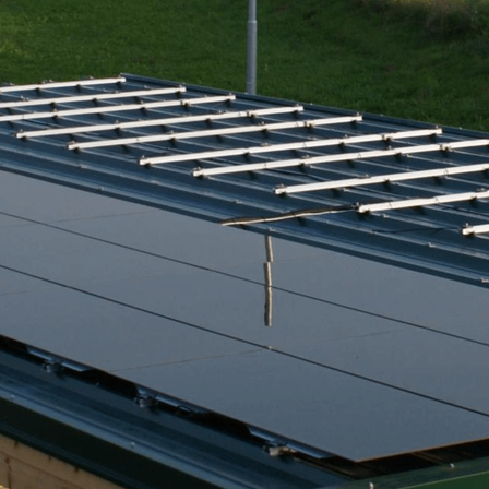 Ein Nahaufnahme eines Solarpanelsystems, das auf einem Metalldach montiert ist und den Himmel und das Gras reflektiert.