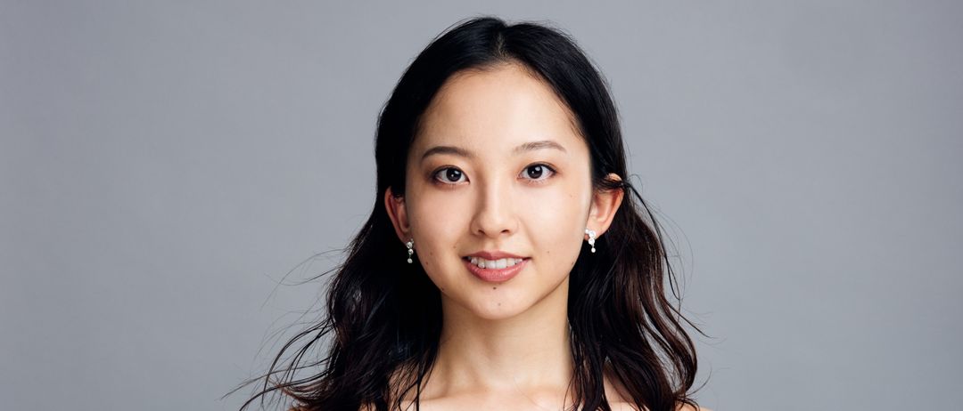 Eine Frau mit langen dunklen Haaren in einem schwarzen Kleid lächelt, während sie ein Cello hält.