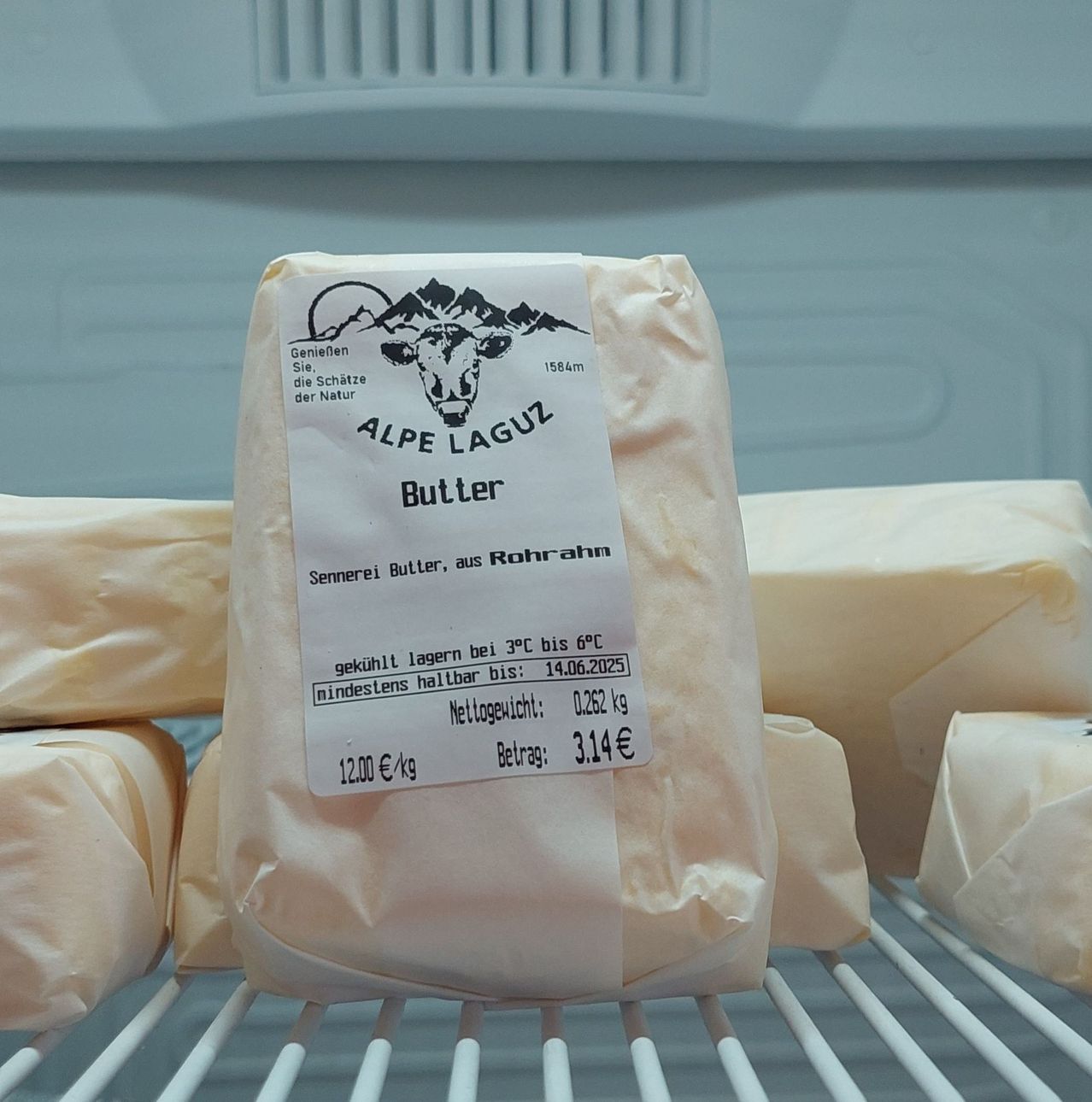 Eine Packung Alpe Laguz Butter, in Papier eingewickelt, wird gekühlt aufbewahrt mit einem Nettogewicht von 0,262 kg und einem Preis von 3,14 Euro pro kg.