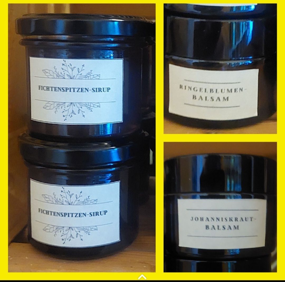 Vier Gläser mit schwarzen Deckeln und weißen Etiketten, die auf einer Holzoberfläche gestapelt sind. Die Etiketten tragen die Aufschriften 'FICHTENSPITZEN-SIRUP', 'RINGELBLUMEN-BALSAM' und 'JOHANNISKRAUT-BALSAM'. Sie haben florale Designs.