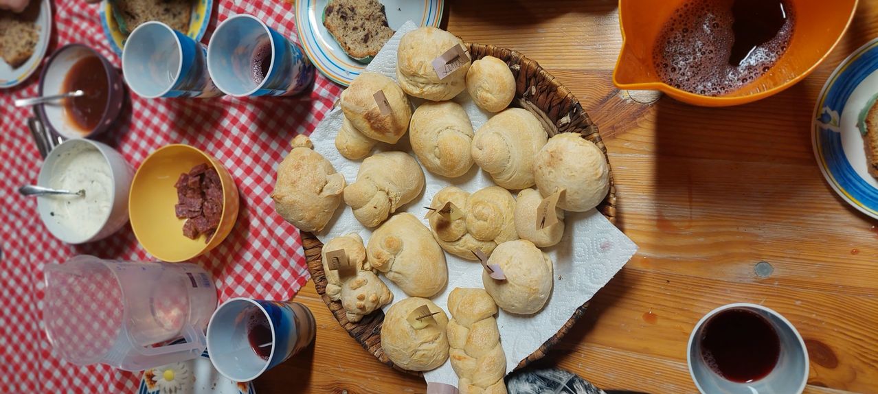A basket of golden brown pastries, some with tags, sits on a table with a red and white checkered tablecloth. Two cups with red liquid are nearby.