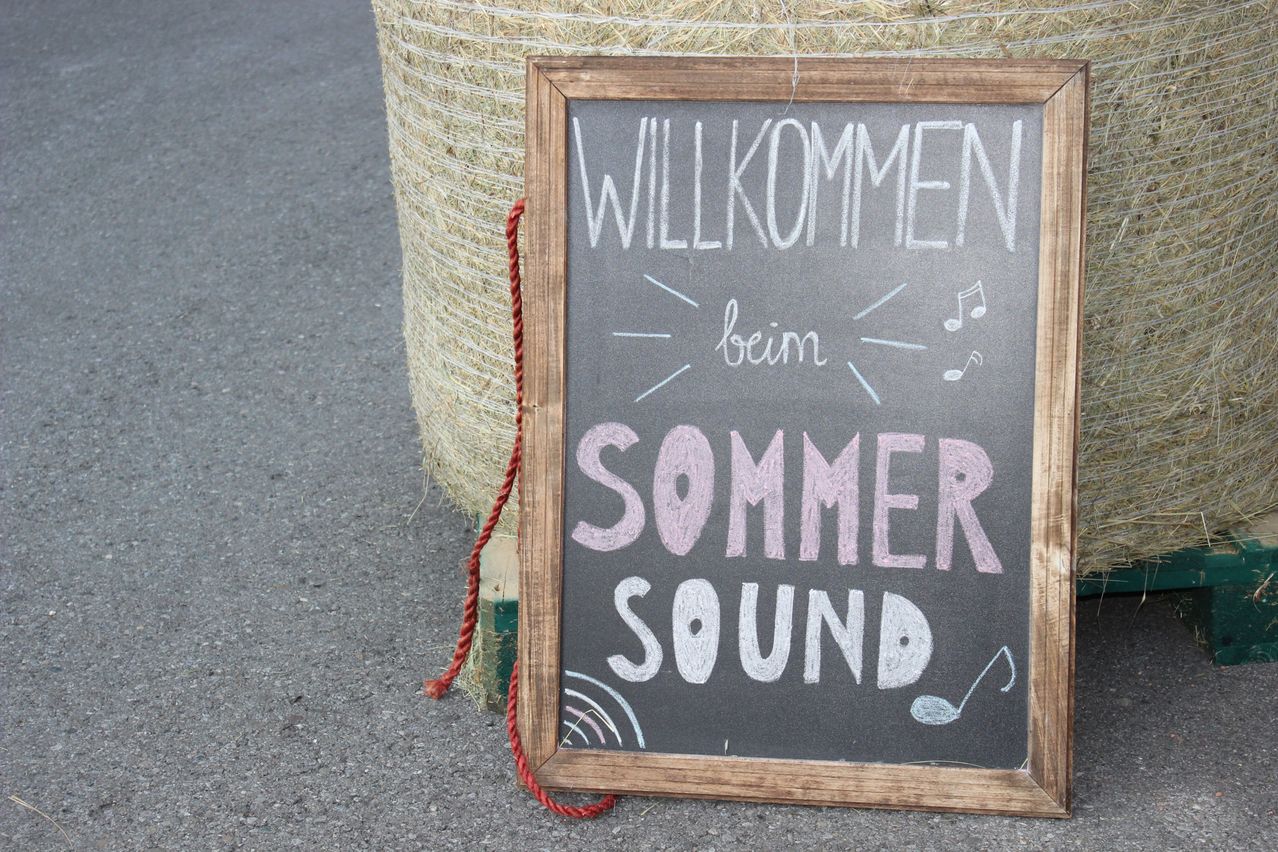 A wooden framed chalkboard with a message written in chalk, 'Willkommen beim Sommer Sound', with musical notes around it.