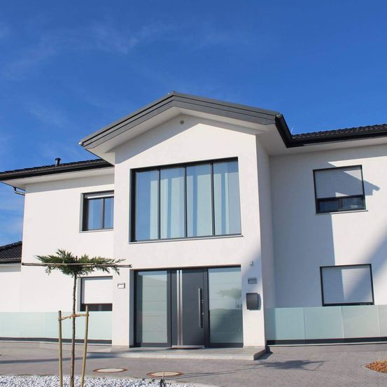 Ein modernes weißes Haus mit schwarzem Dach und Glasfenstern, mit einer großen Vordertür mit grauem Rahmen.