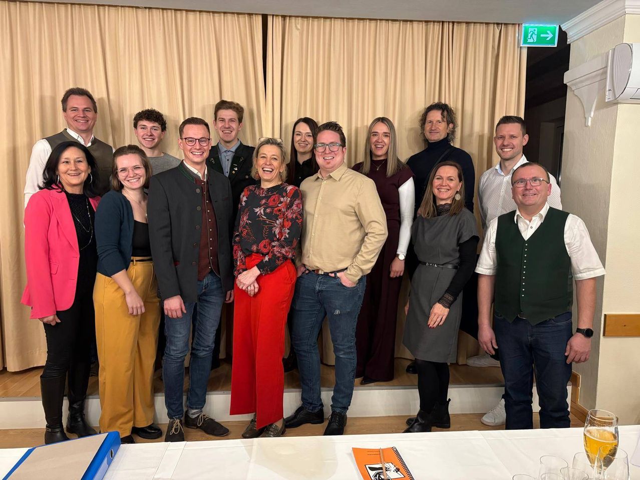 Eine Gruppe von Menschen, wahrscheinlich Kollegen, posiert für ein Foto im Innenbereich. Sie stehen hinter einem Tisch mit beigefarbenen Vorhängen als Hintergrund.