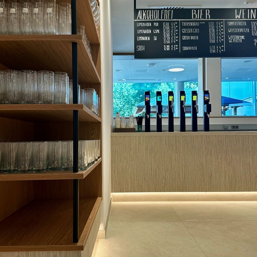 A bar counter with a menu board listing various drinks. The menu board has sections for alcohol-free, beer, and wine. The counter has several taps for beer and wine.