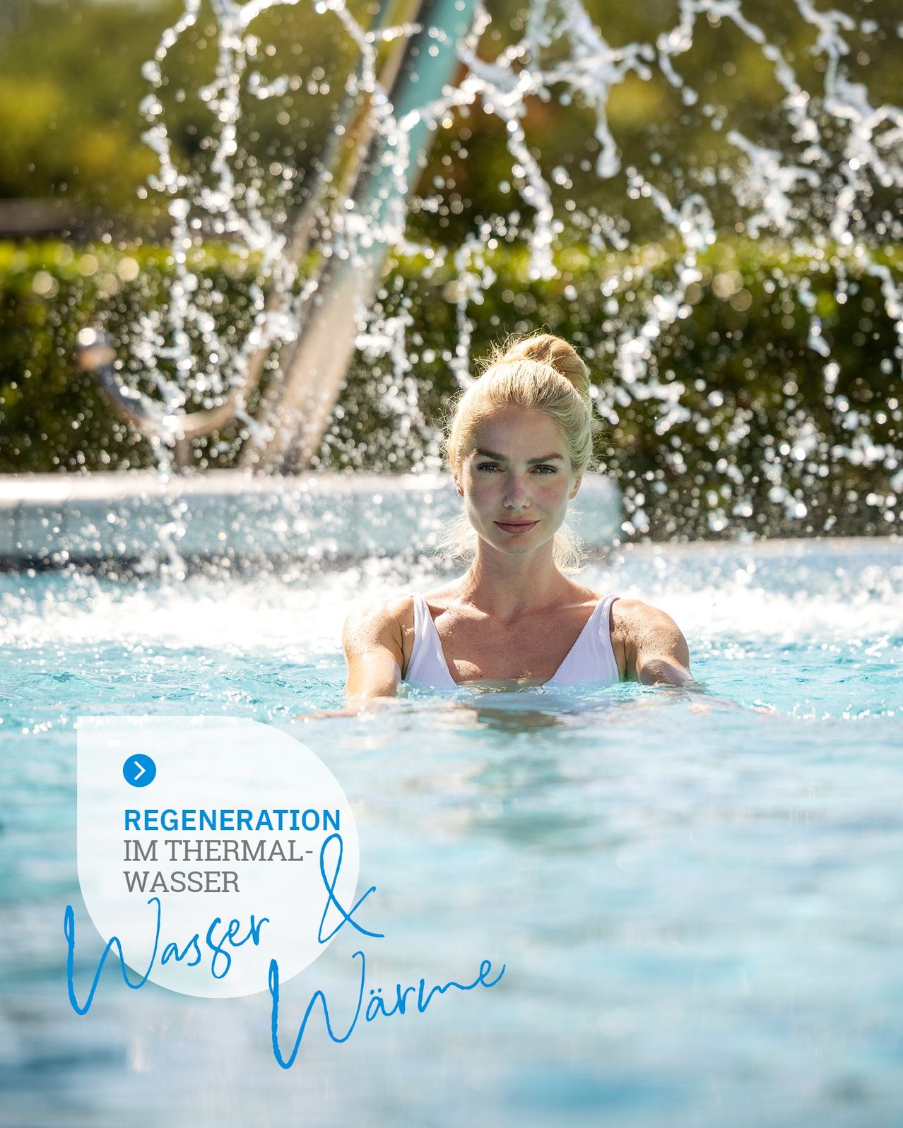 Eine Frau mit blonden Haaren schwimmt in einem Pool, um den herum Wasser spritzt. Der Pool hat einen blauen Rand und ist von Grün umgeben.