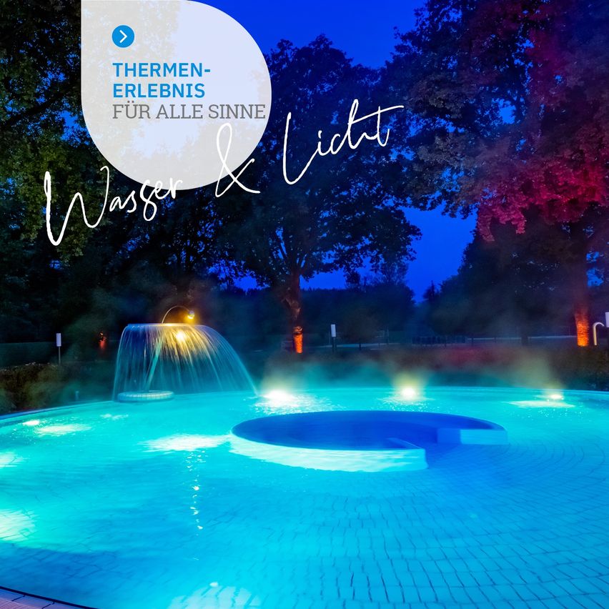 Ein Schwimmbad mit blauem Wasser und einem Brunnen in der Mitte, beleuchtet von blauen Lichtern. Der Pool ist von Bäumen umgeben und hat ein Schild, das 'Thermen-Erlebnis für alle Sinne' besagt.