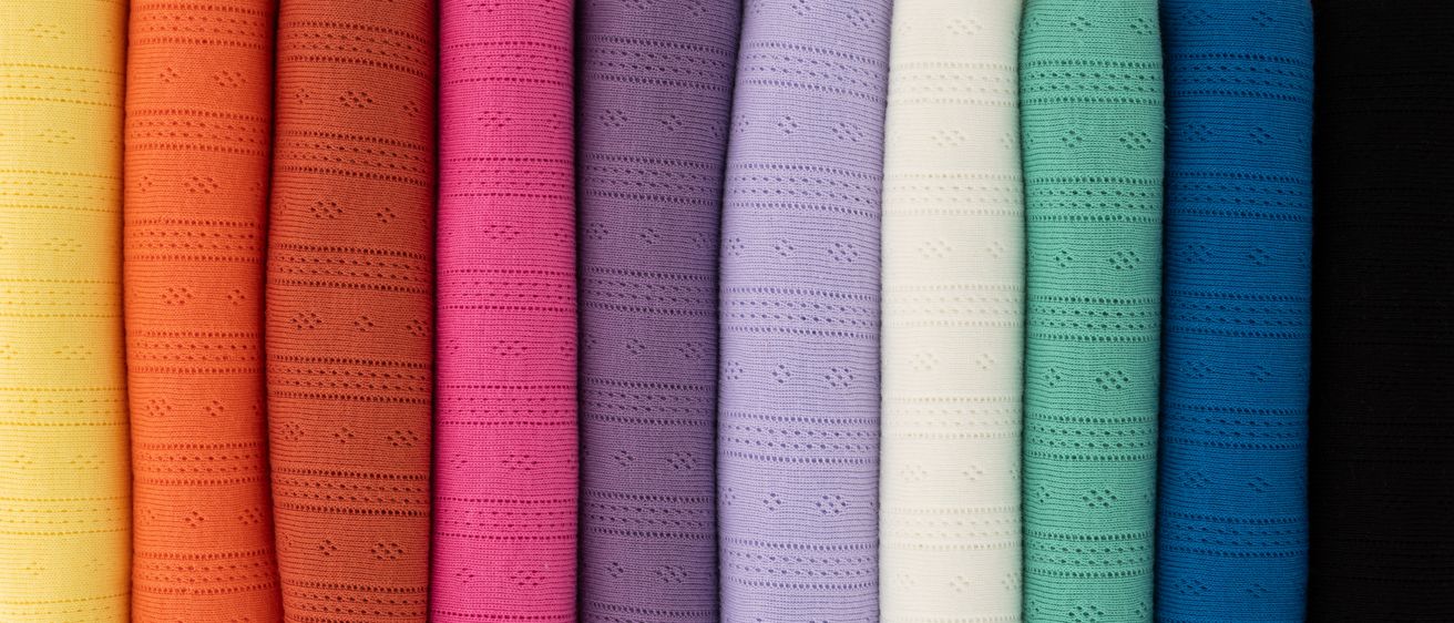 Eine Sammlung von gestrickten Stoffen in verschiedenen Farben wie pink, lila, weiß, grün und orange, in einer Reihe angeordnet. Jeder Stoff weist ein einzigartiges Muster auf.