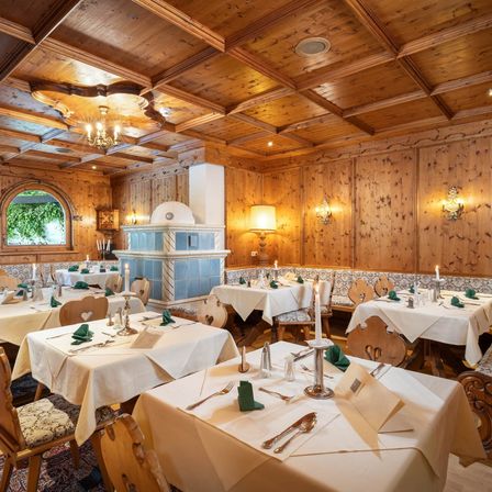 Ein elegant eingerichtetes Esszimmer mit Holzwänden und -decken, das einen Kamin, eine Kronleuchter und mehrere Tische mit weißen Tischdecken und ordentlich geordnetem Besteck aufweist.