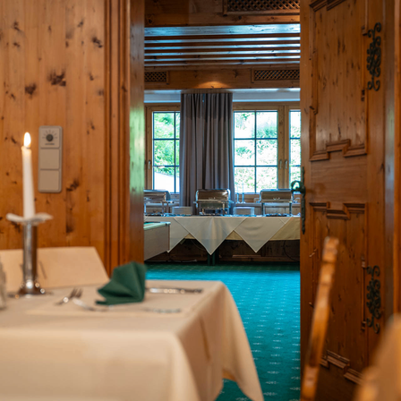 Ein Restaurant-Interieur mit Holzwänden, einer Kerze auf einem Tisch und Blick auf einen Essbereich mit Tischen und Stühlen.