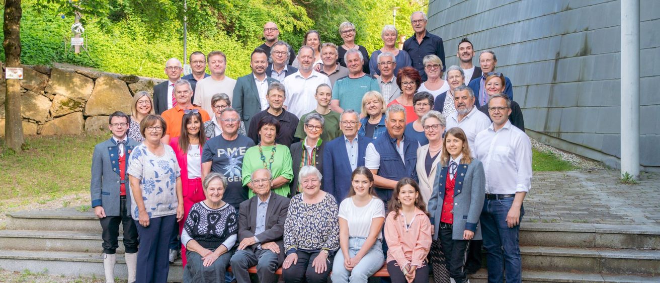 Eine Gruppe von Menschen in verschiedenen Outfits, darunter einige in formeller Kleidung, versammelt sich vor einem großen Gebäude, möglicherweise für ein Foto.