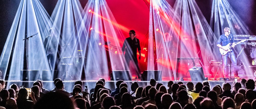 Ein Live-Auftritt auf der Bühne mit roten und weißen Lichtern, ein Mann singt und ein Publikum schaut zu.