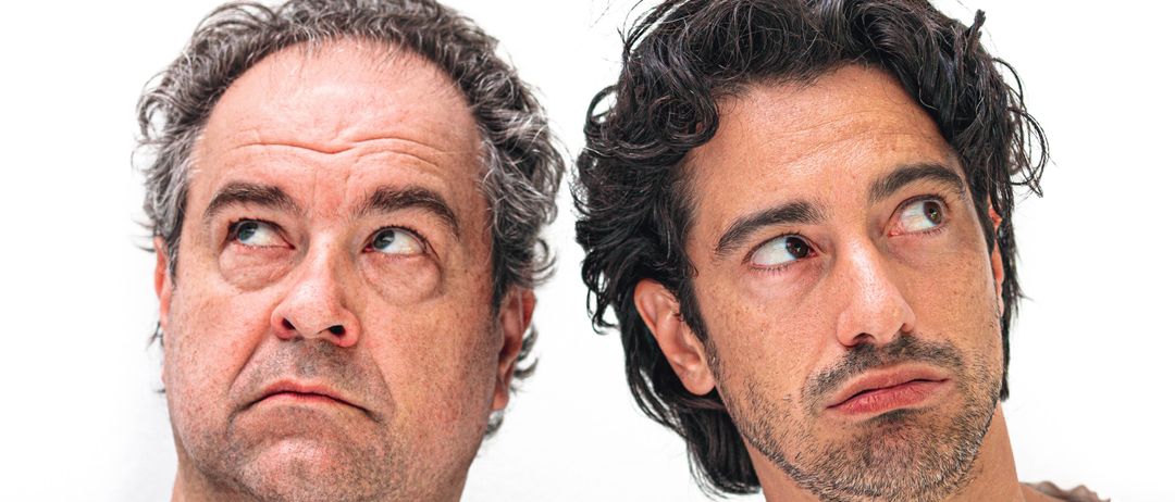 Zwei Männer posieren mit ernster Miene für ein Foto, einer trägt ein schwarzes T-Shirt und der andere ein weißes.