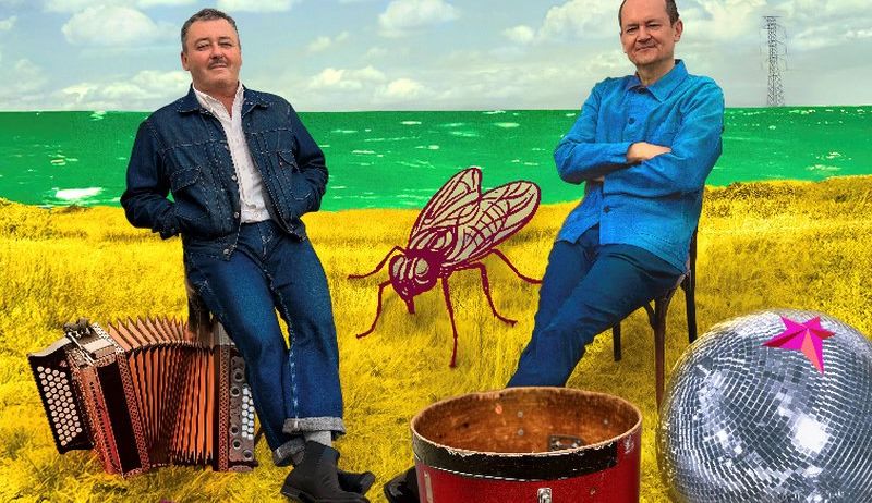 Zwei Männer sitzen auf einem gelben Feld mit Musikinstrumenten um sie herum. Einer hat ein Akkordeon und der andere einen Trommel. Ein rotes Moskito und eine Discokugel sind in der Nähe.