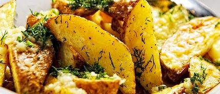 Eine weiße Schüssel mit knusprigen gebratenen Kartoffelstücken, überzogen mit Kräutern, serviert mit einem Löffel.