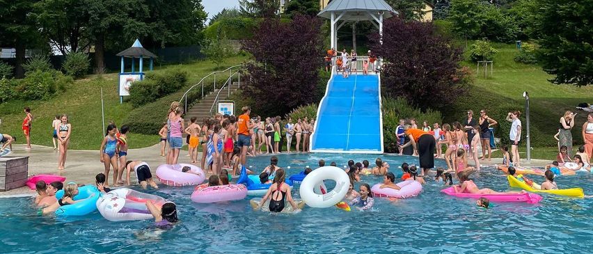 Eine große Gruppe von Kindern genießt einen Wasserpark. Sie schwimmen und spielen im Pool mit Rutschen und aufblasbaren Spielzeugen.