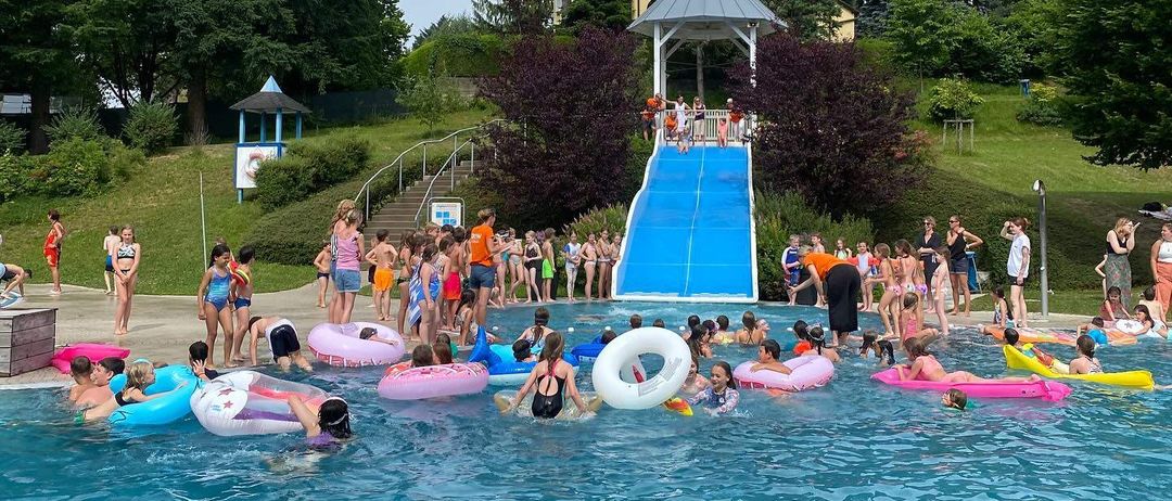 Eine große Gruppe von Kindern genießt einen Wasserpark. Sie schwimmen und spielen im Pool mit Rutschen und aufblasbaren Spielzeugen.