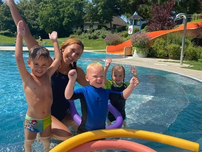 Eine Frau und ihre drei kleinen Kinder haben Spaß in einem Schwimmbad, mit farbigen Ringen, die um sie herum schwimmen.