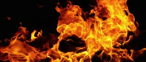 Ein Feuer brennt mit orangen und gelben Flammen vor einem dunklen Hintergrund. Die Hitze und das Licht des Feuers beleuchten die Umgebung.