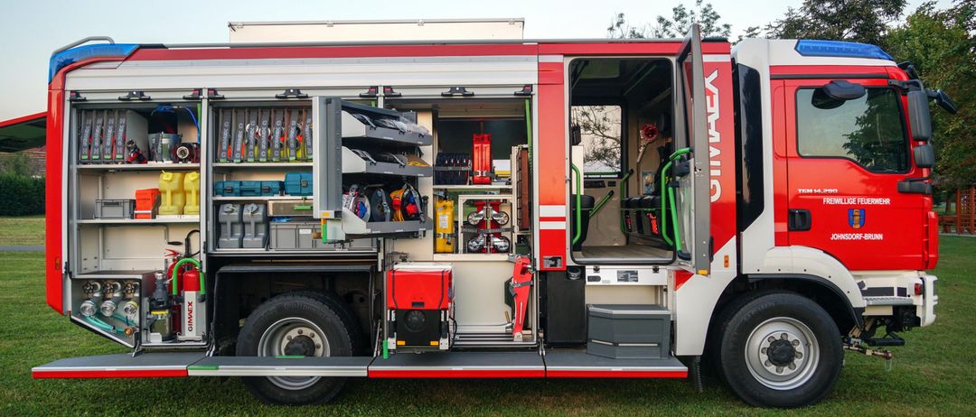 Die Rückansicht eines roten und weißen Feuerwehrwagens mit offenen Türen, die verschiedene Werkzeuge und Ausrüstung auf Regalen zeigt.