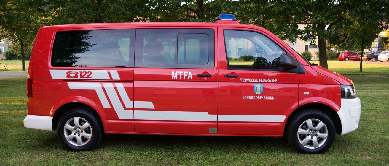 Ein roter Feuerwehrwagen mit MTFA und Johnsdorf-Brunn an der Seite steht auf dem Rasen.