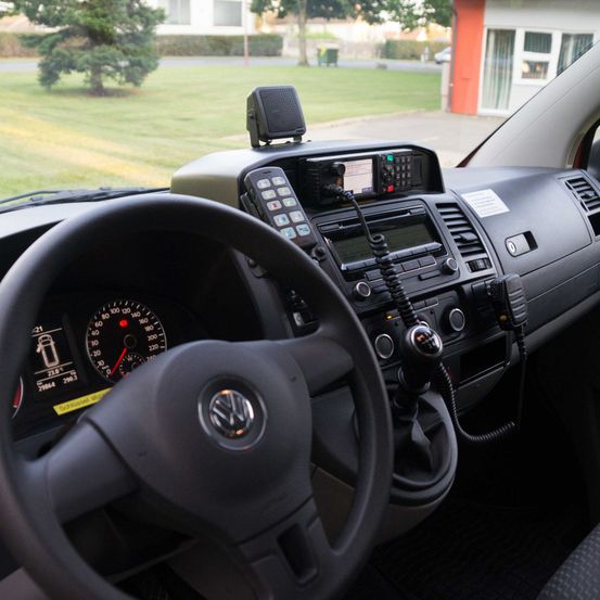 Ein Nahaufnahme der Innenausstattung eines Autos, die das Lenkrad, das Armaturenbrett und das Bedienfeld mit verschiedenen Knöpfen und einem Radio zeigt.