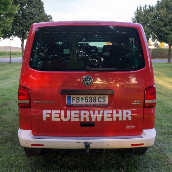 Die Rückseite eines roten Volkswagen Caravelle-Vans steht auf einem Rasenfeld. Er hat ein Nummernschild mit der Aufschrift FB 538 CS. Das Wort Feuerwehr ist in weiß auf der Rückseite geschrieben.