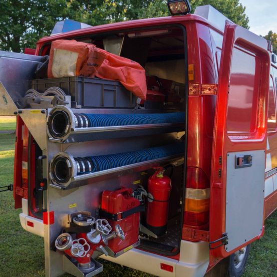 Die Rückseite eines roten Feuerwehrwagens ist geöffnet und zeigt Feuerlöscher, Schläuche und Werkzeuge im Inneren.