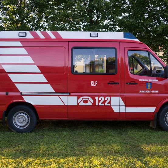 Ein roter Feuerwehrwagen mit weißen Streifen und der Nummer 122 in einem Grasbereich in der Nähe eines Baumes und Gebäudes geparkt.