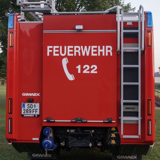 Ein roter Feuerwehrwagen mit der Aufschrift 'FEUERWEHR' und '122' steht auf einer Wiese. Der Wagen hat eine Leiter, ein Kennzeichen SO 289 FF und den Herstellernamen GIMAX.