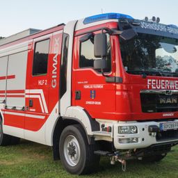 Ein roter Feuerwehrwagen mit der Aufschrift GIMAX und den Texten 'HLF 2' und 'JOHNSORP-BRUUN' steht auf grünem Gras. Das Kennzeichen lautet 'SO 289 FF'.