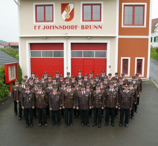 Eine Gruppe uniformierter Feuerwehrleute posiert für ein Foto vor der Feuerwehrstation F.F. Johnsdorf-Brunn.