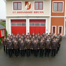 Eine Gruppe uniformierter Feuerwehrleute posiert für ein Foto vor der Feuerwehrstation F.F. Johnsdorf-Brunn.