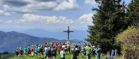 Eine Menschenmenge steht auf einem grasbewachsenen Hügel, mit einem Kreuz in der Mitte. Einige Menschen halten Musikinstrumente.