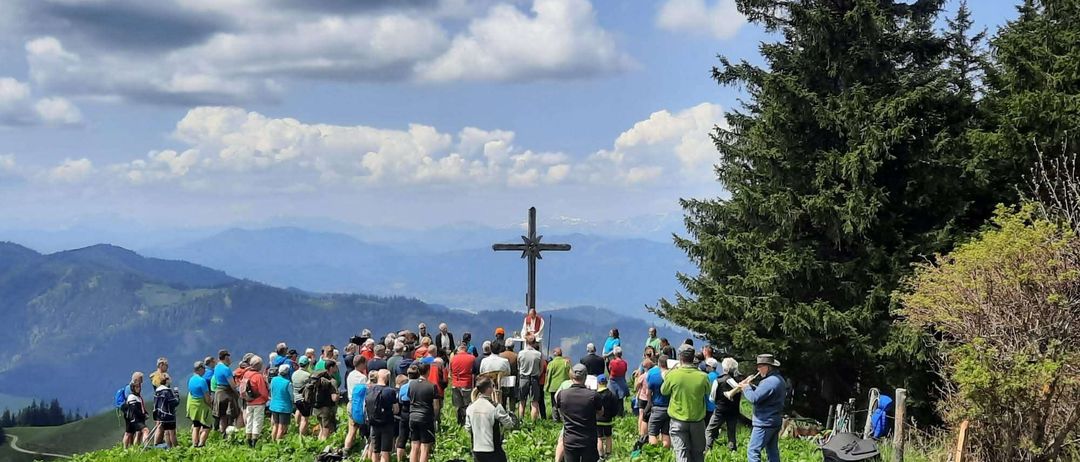 Eine Menschenmenge steht auf einem grasbewachsenen Hügel, mit einem Kreuz in der Mitte. Einige Menschen halten Musikinstrumente.