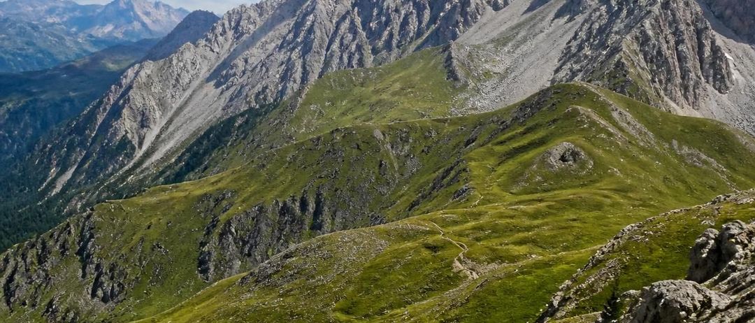 Ein Panoramablick auf eine Berglandschaft mit üppigen grünen Tälern und felsigen Gipfeln unter einem teilweise bewölkten Himmel.