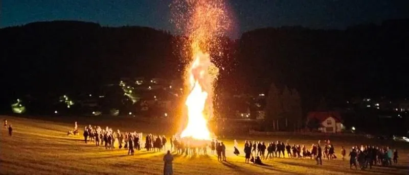 Ein großes Lagerfeuer brennt in der Mitte eines Feldes bei Nacht. Viele Menschen sind darum herum versammelt, möglicherweise für eine Feier.