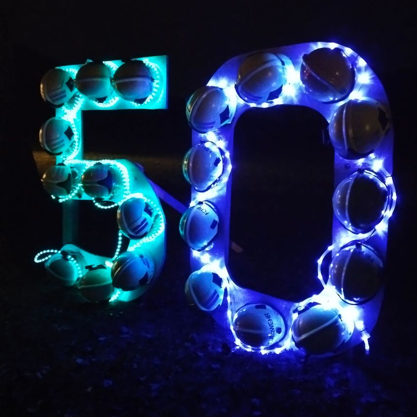 Die Zahl 50 besteht aus leuchtenden blauen und grünen LED-Lichtern, geformt wie Helme mit einer reflektierenden Oberfläche.