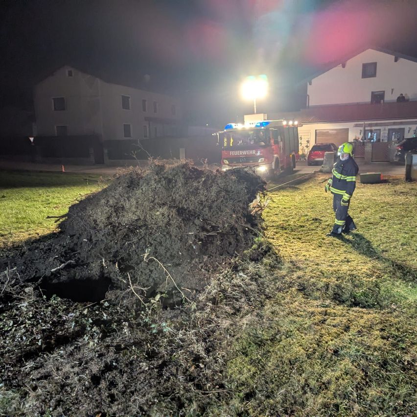 In der Nacht steht ein Feuerwehrmann neben einem großen Haufen Erde, mit einem Feuerwehrwagen in der Nähe und einem Haus im Hintergrund.
