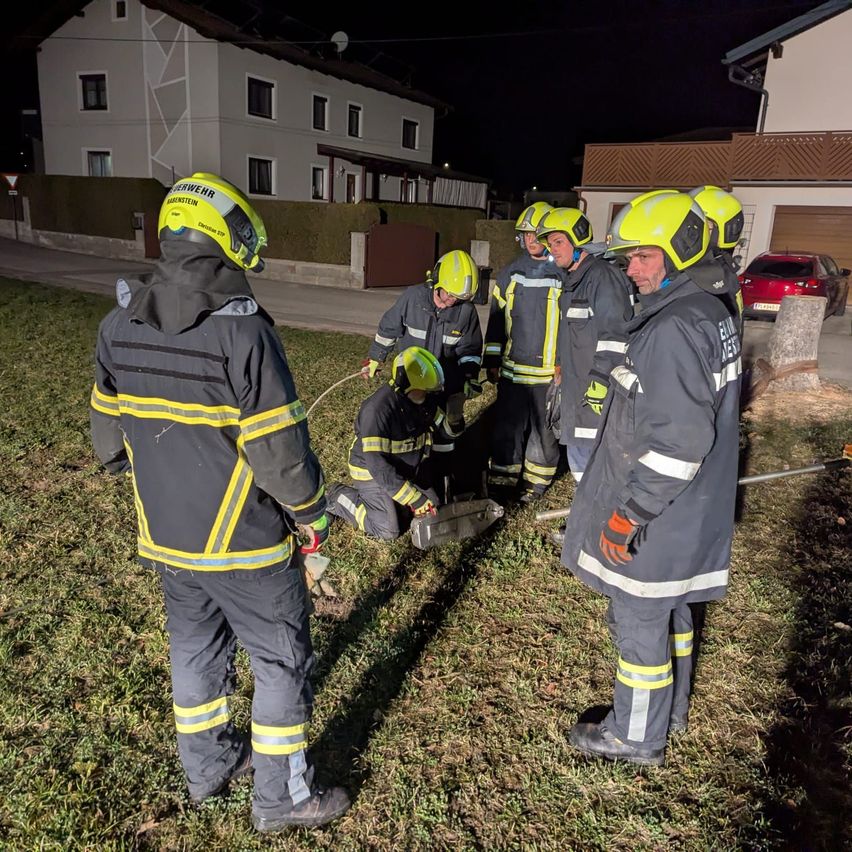 Feuerwehrleute arbeiten vor einem Haus auf dem Boden und tragen Helme und Schutzanzüge. Sie suchen wahrscheinlich nach etwas. Das Haus ist von Straßenlaternen beleuchtet.