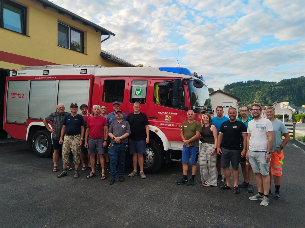 Eine Gruppe von Menschen, möglicherweise Feuerwehrleute, posiert für ein Foto vor einem roten Feuerwehrauto.