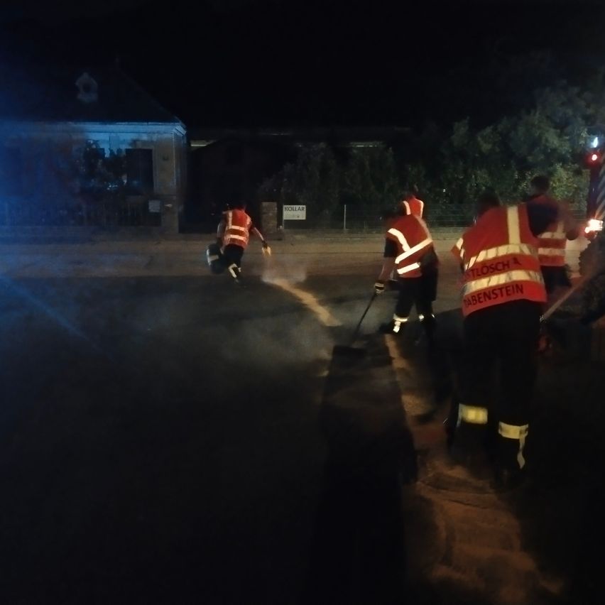 Vier Arbeiter in Warnwesten reinigen die Straße bei Nacht, mit einem Gebäude und Bäumen im Hintergrund.