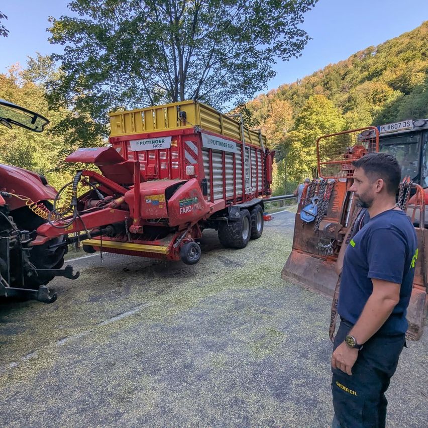 Ein Mann in einem blauen T-Shirt steht neben einem roten Traktor mit gelbem Dach. Der Traktor ist am Straßenrand geparkt.