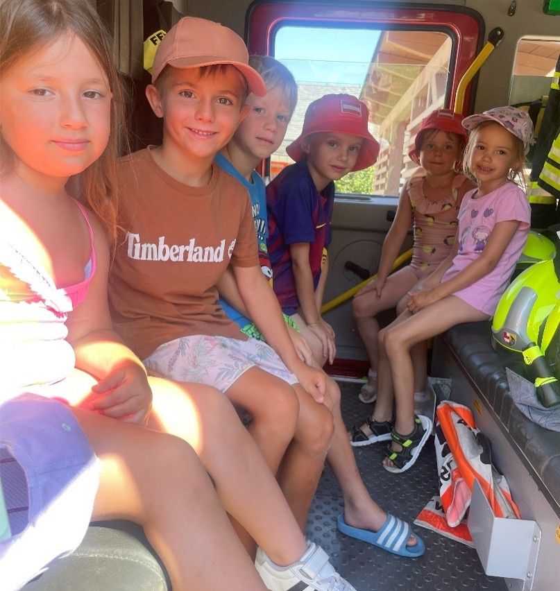 Fünf Kinder sitzen lächelnd und posieren für ein Foto im Inneren eines Feuerwehrwagens. Der Junge in der Mitte trägt ein Timberland-Shirt.