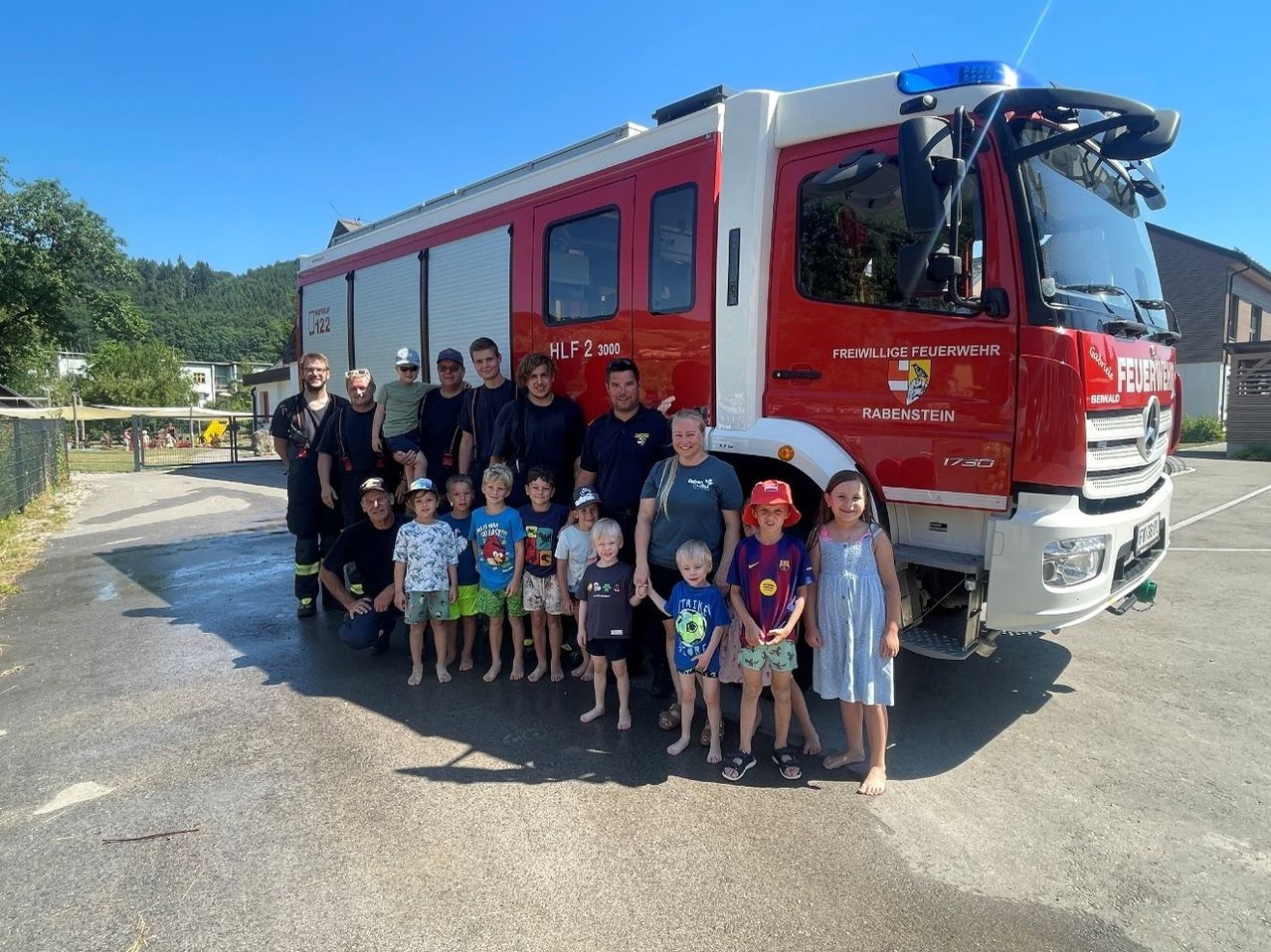 Eine Gruppe von Feuerwehrleuten und Kindern posiert vor einem roten Feuerwehrauto mit der Aufschrift 'Freiwillige Feuerwehr Rabenstein' an der Seite.