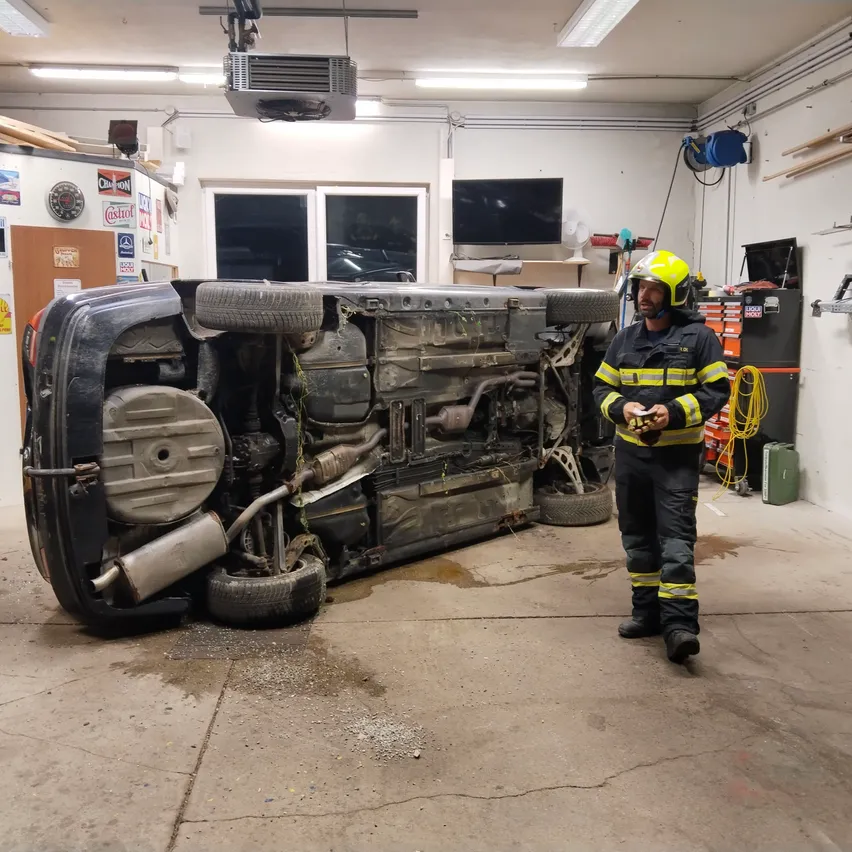 Ein Feuerwehrmann steht neben einem umgestürzten Auto in einer Garage.